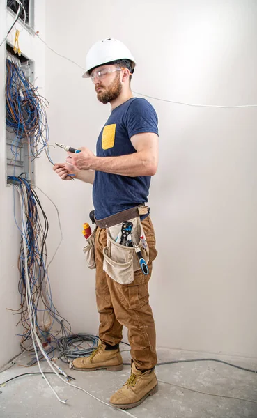 Electrician Builder at work, examines the cable connection in the electrical line in the fuselage of an industrial switchboard. Professional in overalls with an electrician\'s tool. The concept of working as a professional.