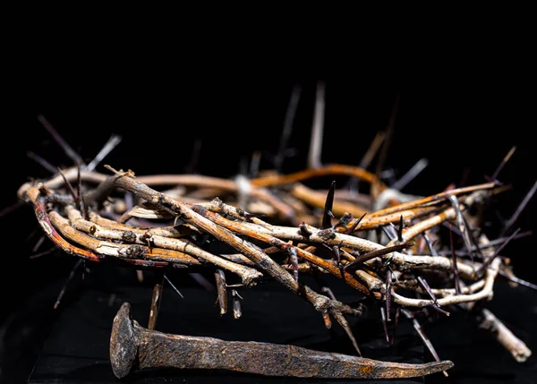 A crown of thorns and an old rusty nail lie on an isolated black background. The concept of Holy week.