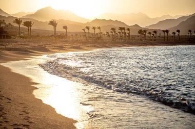 Gün batımında güzel kumlu sahil. Dağın arka planında deniz dalgaları var..