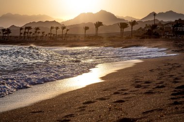 Gün batımında güzel kumlu sahil. Dağın arka planında deniz dalgaları var..