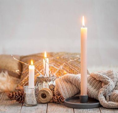 Evin içi sıcacık, yanan mumlar, ahşap bir masa üzerindeki sıcak süveter. Mevsimlik sonbahar-kış konsepti rahat bir ev, asgari dekorasyon, ısınma.