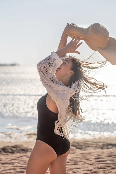 Şapkalı ve mayolu güzel bir kadın deniz kenarında sahilde yürüyor..