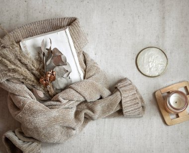 Sıcak pastel süveter ve mum manzaralı kurutulmuş çiçek buketi, sonbahar samimiyeti kavramı.