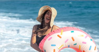 Deniz kenarında çörek şeklinde bir yüzme çemberi olan neşeli bir kadın. Boş zaman ve eğlence kavramı.