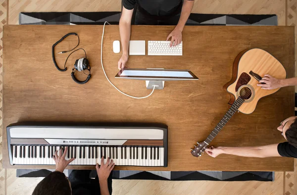 Musician creating music in his studio playing a musical keyboard and acoustic guitar. Process of working on sound on wooden table background copy space