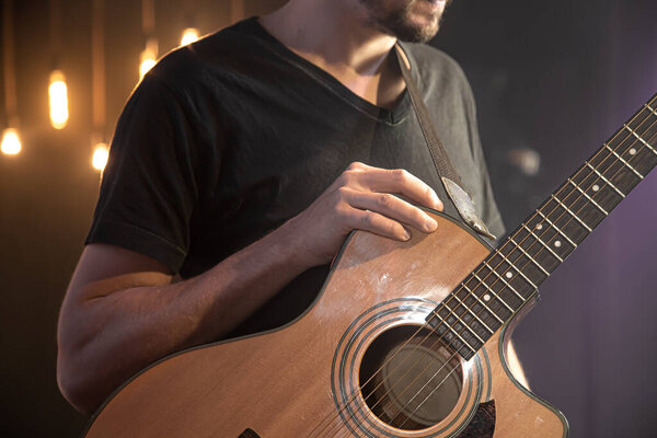 Acoustic guitar in the hands of a guitarist at a concert close-up on a black blurred background close up.