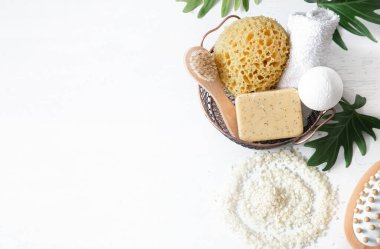 Banyo aksesuarlarıyla dolu bir hayat. Sepette bir bez, bir sabun fırçası, bir havlu, beyaz deniz tuzu beyaz arka plan fotokopi alanı, üst görünüm.