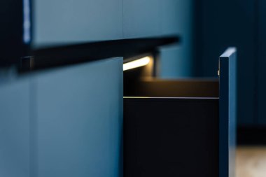 Çekmecenin içinde yumuşak LED ile mat mavi modüller boyunca perspektif görünümü. Derinlik, gölgeler ve kısıtlı biçimler minimalist stili vurguluyor.