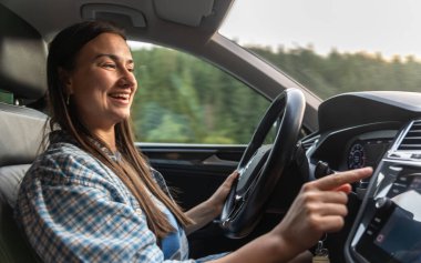 Navigasyon ekranına basarken kareli gömlekli genç bir kadın araba kullanıyor. Neşe atmosferi, özgürlük ve modern yaşam tarzı yolda.