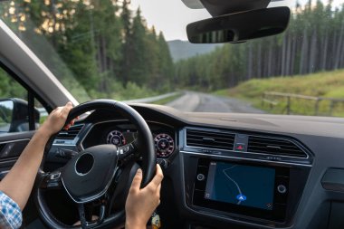 Elleri direksiyonda ve seyrüsefer ekranında olan bir orman yolunda giderken bir arabanın iç görüntüsü. Macera atmosferi, sakinlik ve seyahat.