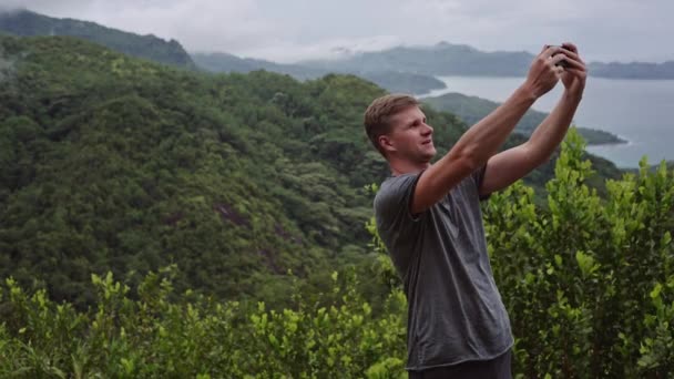 Um jovem falando ao telefone por videochamada, em pé no topo de uma colina verde . — Vídeo de Stock