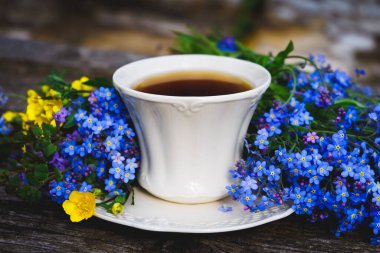 Beyaz renkli seramik bardakta bitki çayı, tahta bir arka planda taze unutma beni çiçekleri.