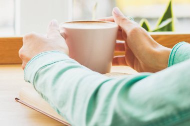 Kadın bir fincan kapuçino ellerini, yumuşak odak arka plan ile