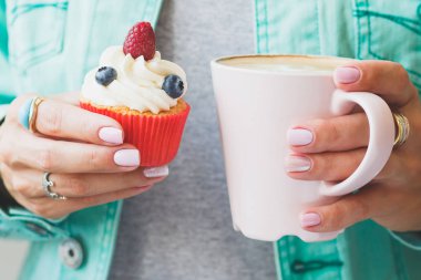 Bir fincan kapuçino ve cupcake ellerini, yumuşak odak arka plan kadınla