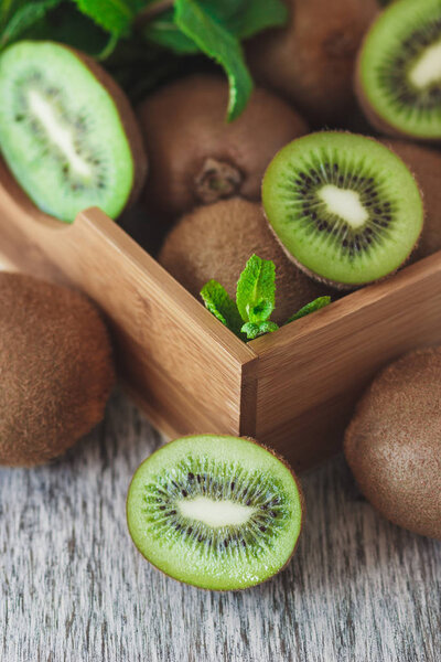 Green kiwis and mint leaves in the wooden tray, soft focus background