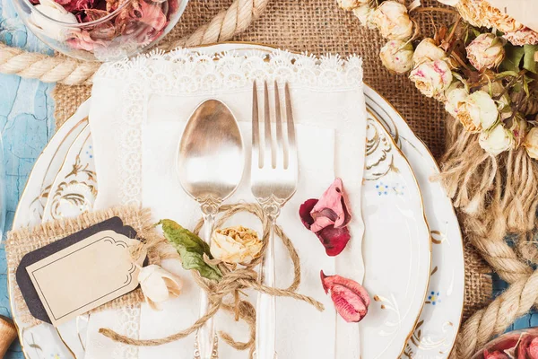 Sofra ve kuru çiçekler ve mavi eski ahşap arka plan üzerinde farklı süslemeler ile Gümüş eşyalar