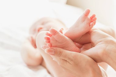 Kadının elleri bebek ayaklarını tutuyor, yumuşak odaklı arka plan