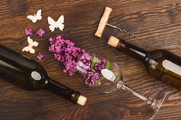 Wineglass with lilacs, bottles and butterflies decorations on the wooden background