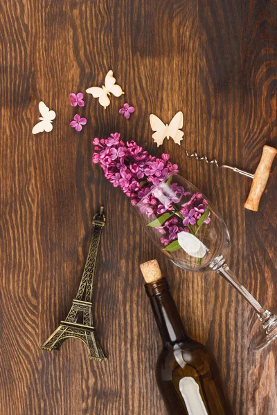 Bottle of wine, wineglass with lilacs and decorations on the wooden background