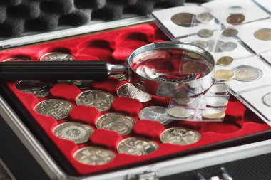 Different collector's coins in the box with a magnifying glass, soft focus background clipart