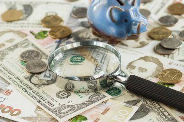 Ukrainian hryvnia and American's dollars with a piggy bank and magnifying glass, soft focus background clipart