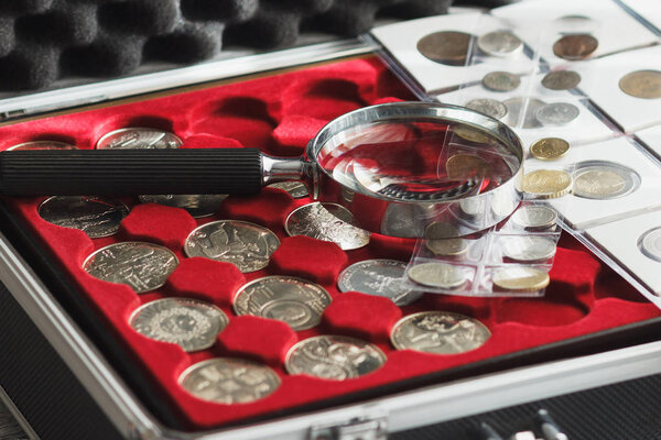 Различные коллекционные монеты в коробке с увеличительным стеклом, мягкий фон фокуса
