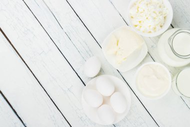 Beyaz ahşap tahtalarda farklı süt ürünleri, üst manzara.