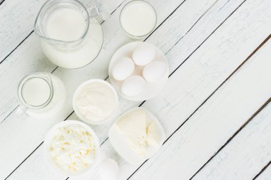 Beyaz ahşap tahtalarda farklı süt ürünleri, üst manzara.
