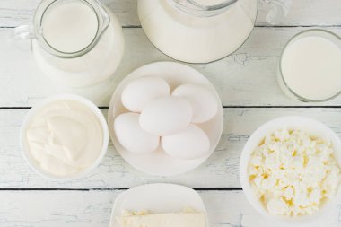 Beyaz ahşap tahtalarda farklı süt ürünleri, üst manzara.