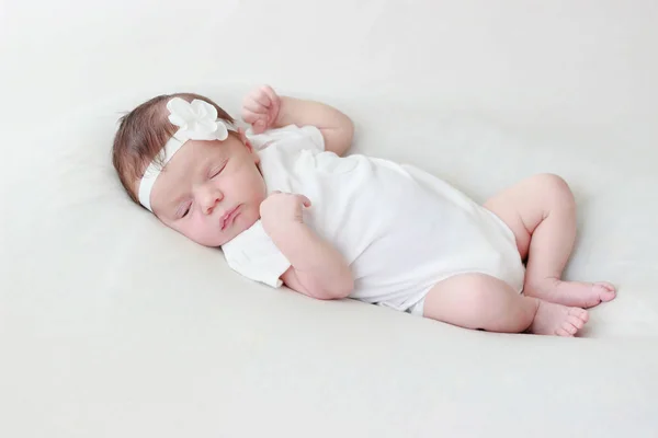 Newborn baby laying on a white blanket, blurred background