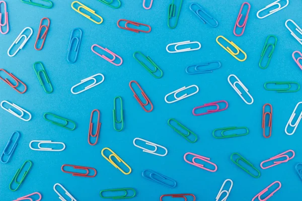 Background made from colored paper clips on the light blue base, top view
