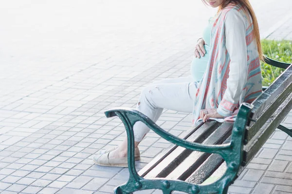 Těhotná žena sedí na lavičce v parku, měkké zaostření pozadí — Stock fotografie