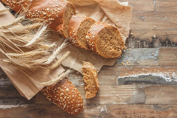 Handmade bread with bran and ears of wheat, wooden background