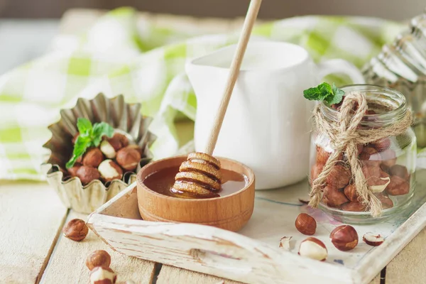 Honung i trä bowl, mynta blad, hasselnötter och burk med mjölk i trä facket — Stockfoto