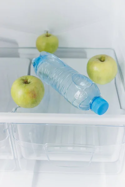 Frigorífico vazio com uma garrafa de água e maçãs verdes na prateleira, conceito de dieta — Fotografia de Stock