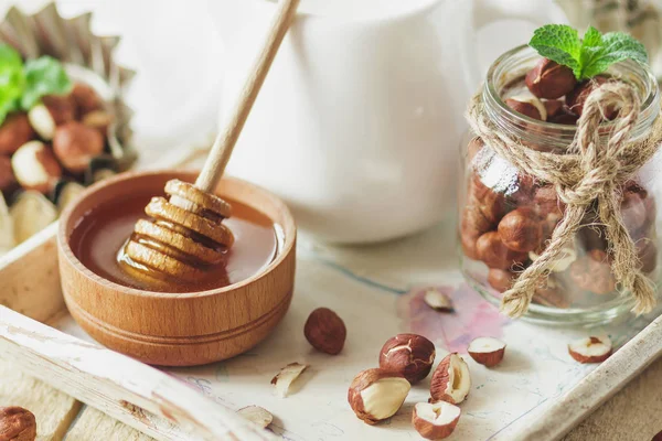 Honung i trä bowl, mynta blad, hasselnötter och burk med mjölk i trä facket — Stockfoto