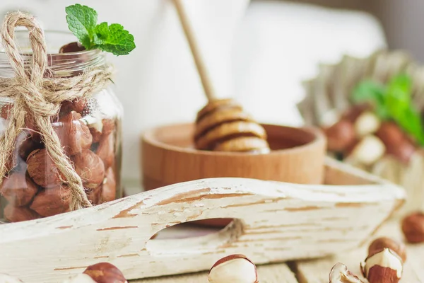 Honung i trä bowl, mynta blad, hasselnötter och burk med mjölk i trä facket — Stockfoto