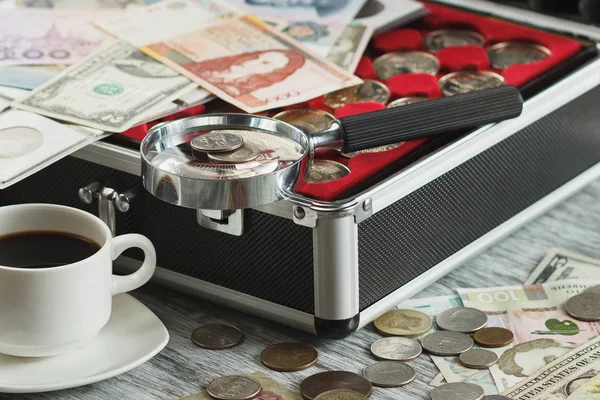Різні колекційні монети та банкноти зі збільшувальним склом, коробка для монет та чашка кави — стокове фото