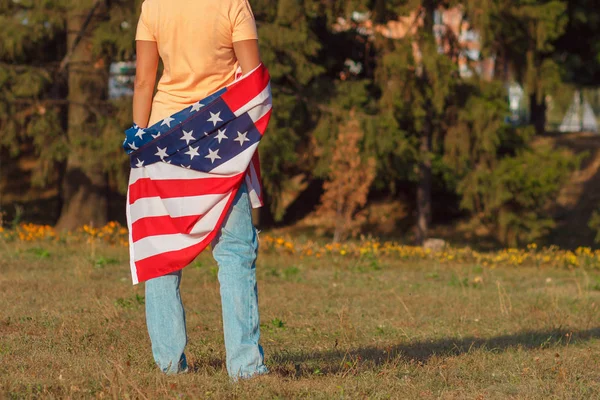 Frau mit einer Flagge der Vereinigten Staaten von Amerika in der Hand, im Freien, Hintergrund mit weichem Fokus — Stockfoto