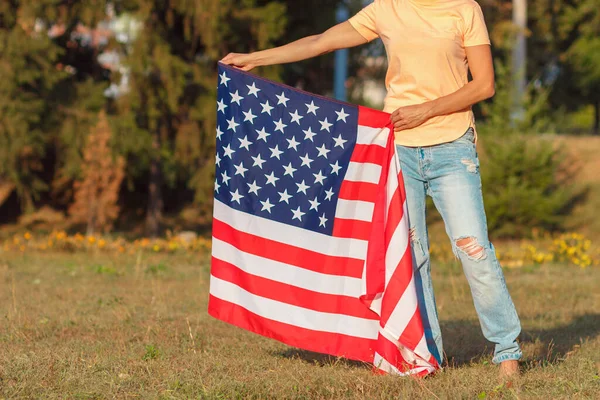 Woman with a flag of United States of America in the hands, outdoors, soft focus background