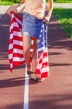 Ellerinde Amerika Birleşik Devletleri bayrağı olan bir kadın, açık havada, yumuşak odaklı arka planda