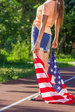 Ellerinde Amerika Birleşik Devletleri bayrağı olan bir kadın, açık havada, yumuşak odaklı arka planda