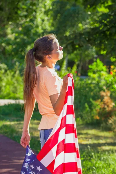Woman with a flag of United States of America in the hands, outdoors, soft focus background