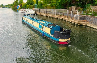 Thames Nehri 'nin su yolunda yüzen kanal teknesi, cennet gibi bir cazibeyi yansıtıyor, dingin ve büyüleyici bir sahne yaratarak sudaki sükunet ve macerayı çağrıştırıyor.