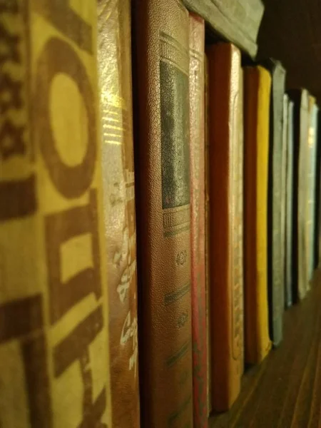Old books in yellow-ocher hues on the shelf, photographed at an angle