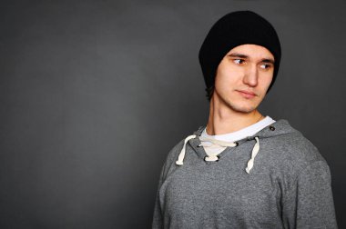 Gri bir hoodie ve siyah bir şapka genç bir adam portresi. Gri bir arka plan üzerinde poz. Stüdyo vurdu.