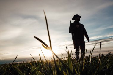 Eski avcı yürüyüşleri. Tüfek Avcısı Silhouetted in Beautiful Sunset or Sunrise. Avcı bataklıkta ve tarlada tüfeği hedefliyor