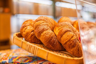 Hasır sepette yeni pişmiş kruvasanlar. Kruvasanlar altın rengi kahverengi ve pul pul. Lezzetli bir pasta sergiliyorlar..