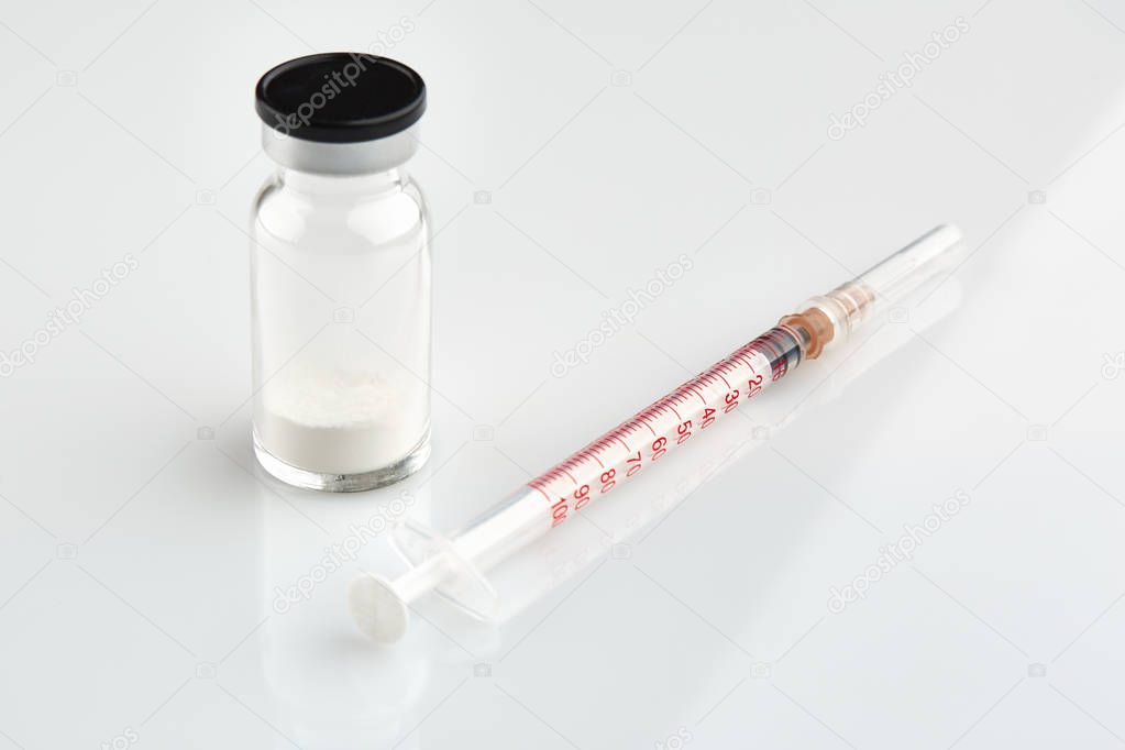 Small sealed bottle with medicine and syringe on white background.