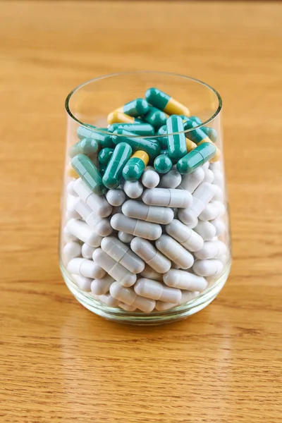 Många vita och gröna piller i genomskinligt glas på trä bakgr — Stockfoto